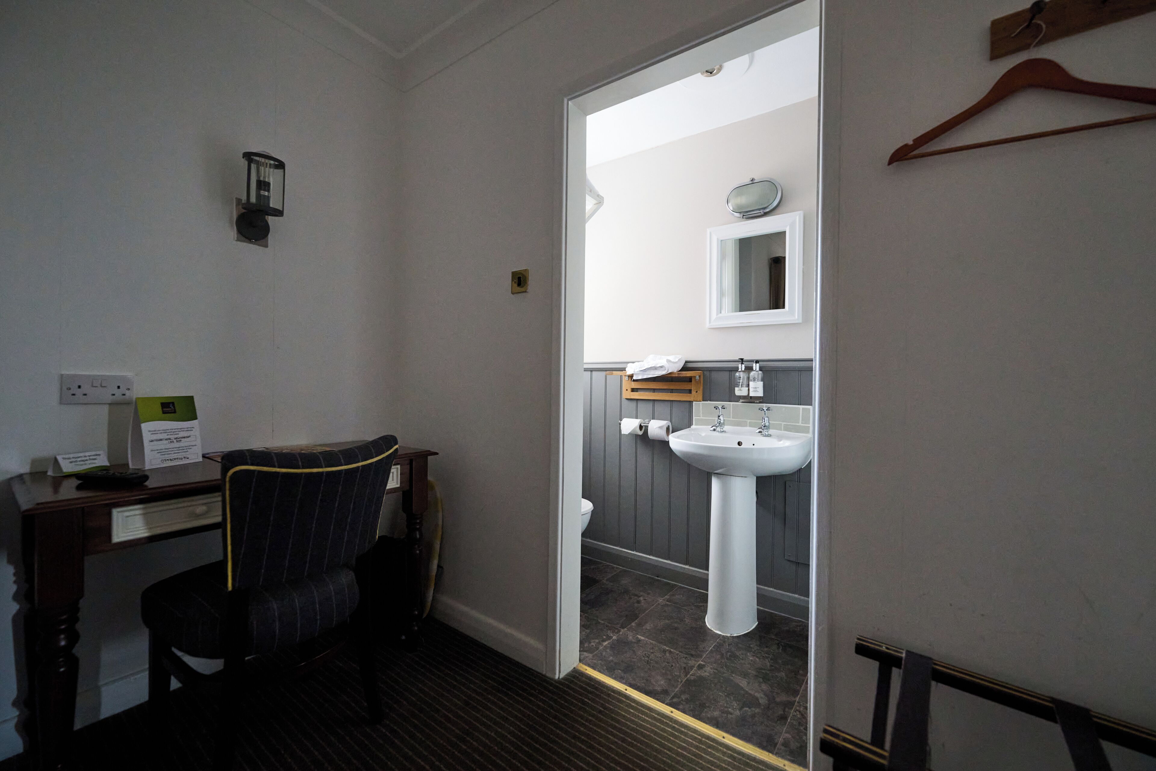 A hotel room with a desk, chair, and a bathroom with a sink and mirror.