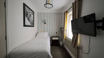 Una habitación de hotel pequeña y ordenada con una cama individual, una mesita de noche, un televisor montado y un cuadro en la pared.