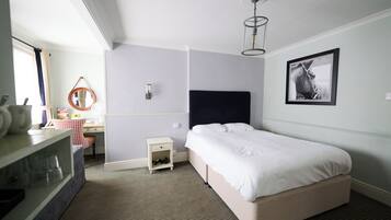 A hotel room with a bed, a desk with a chair, a small bedside table, a mirror, and a framed picture on the wall.