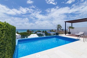 A swimming pool with a clear view of the ocean, surrounded by a white fence and a covered seating area. - Menesse 205 by CocoBR (Playa del Carmen)