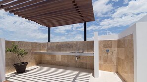 An outdoor bathroom with a built-in sink, a potted plant, and a pergola structure.