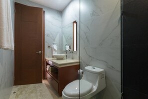 Ein Badezimmer mit einer Marmorwand, einer Holztür, einem weißen Waschbecken und einer Toilette.