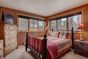 A bedroom with a bed, dresser, TV, windows, and a lamp. - Pines 2045 (Keystone)