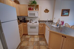 A compact kitchen with wooden cabinets, a white refrigerator, a stove, a microwave, and a sink. - Silver Mill 8227 (Keystone)