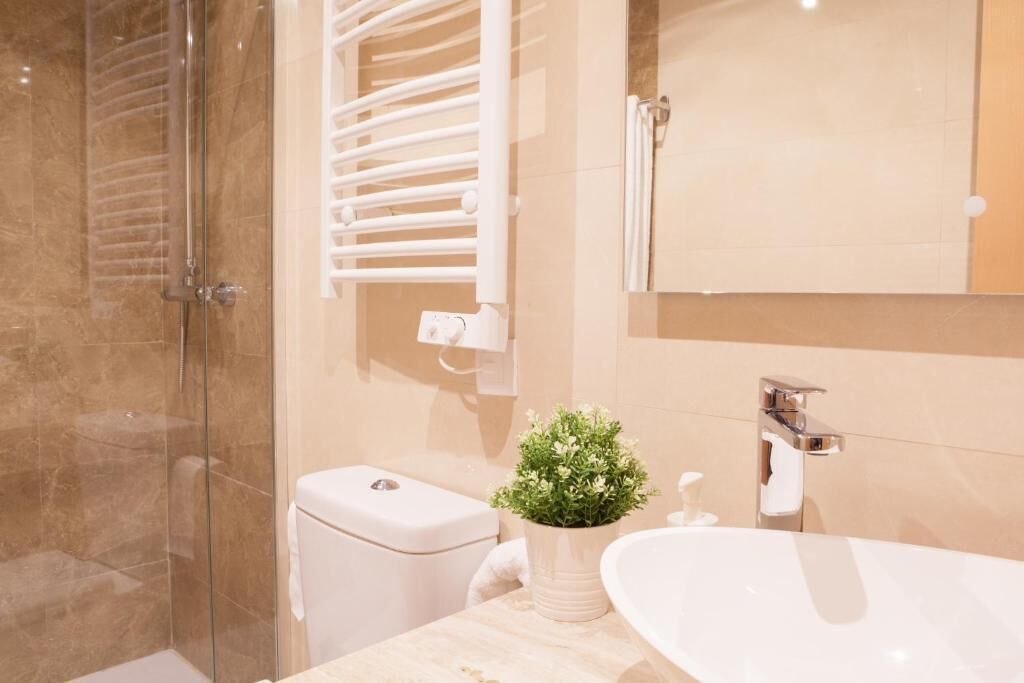 A modern bathroom with a glass shower enclosure, a toilet, a sink with a mirror, and a potted plant.