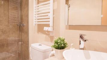 A modern bathroom with a glass shower enclosure, a toilet, a sink with a mirror, and a potted plant.