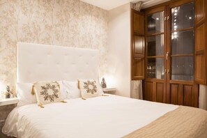 A bedroom with a large bed, a wooden wardrobe, and a window with curtains. - Apartamentos Boutique Salamanca (Salamanca)