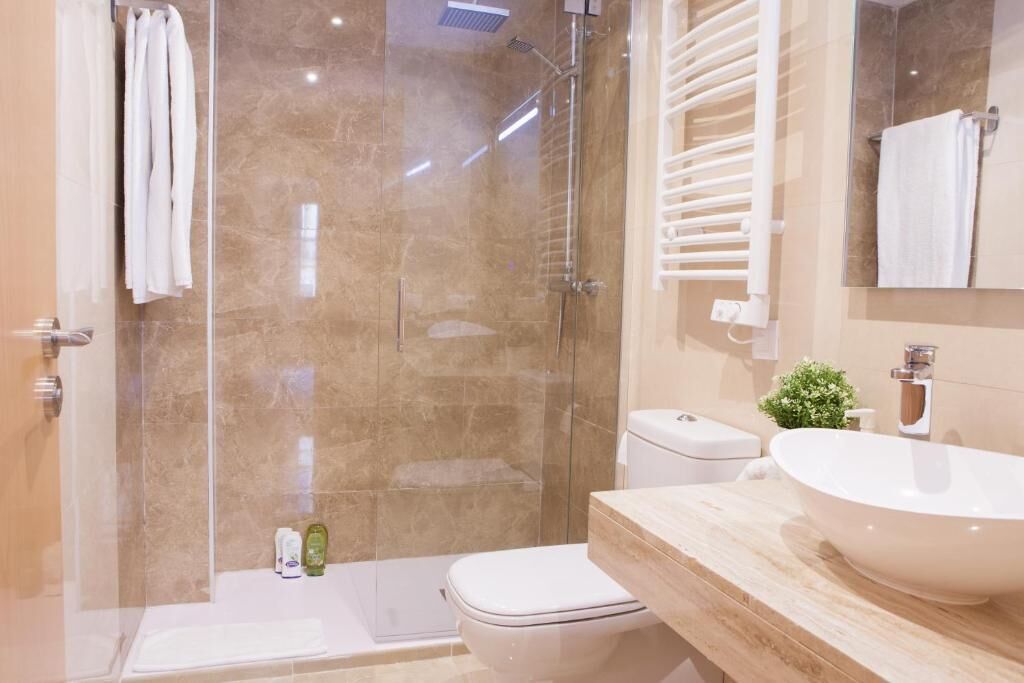 Et moderne badeværelse med et glasafskærmet brusebad, et hvidt toilet, et træbord med en stor vask og et spejl over vasken.