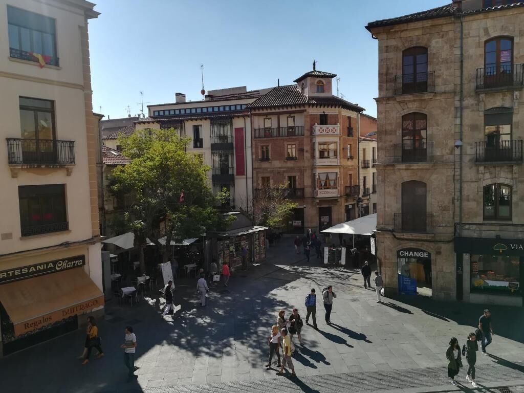 A square with buildings on all sides, outdoor seating, and a few people walking.