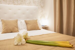 A neatly made bed with white and beige pillows, a beige bedspread, and a bouquet of white flowers and green stems on the bed.