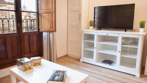 Una sala de estar con un televisor sobre un mueble blanco, una estantería y dos cajas decorativas sobre una mesa.