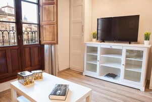 A living room with a TV on a white cabinet, a bookshelf, and two decorative boxes on a table.