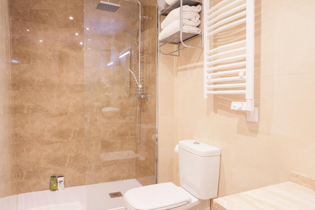 Un bagno con doccia vetro, water e porta asciugamani.