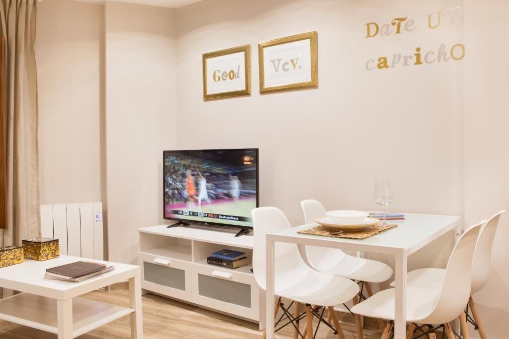 A modern living room with a flat-screen TV, white furniture, and a wall with framed inspirational quotes.