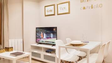 A modern living room with a flat-screen TV, white furniture, and a wall with framed inspirational quotes.