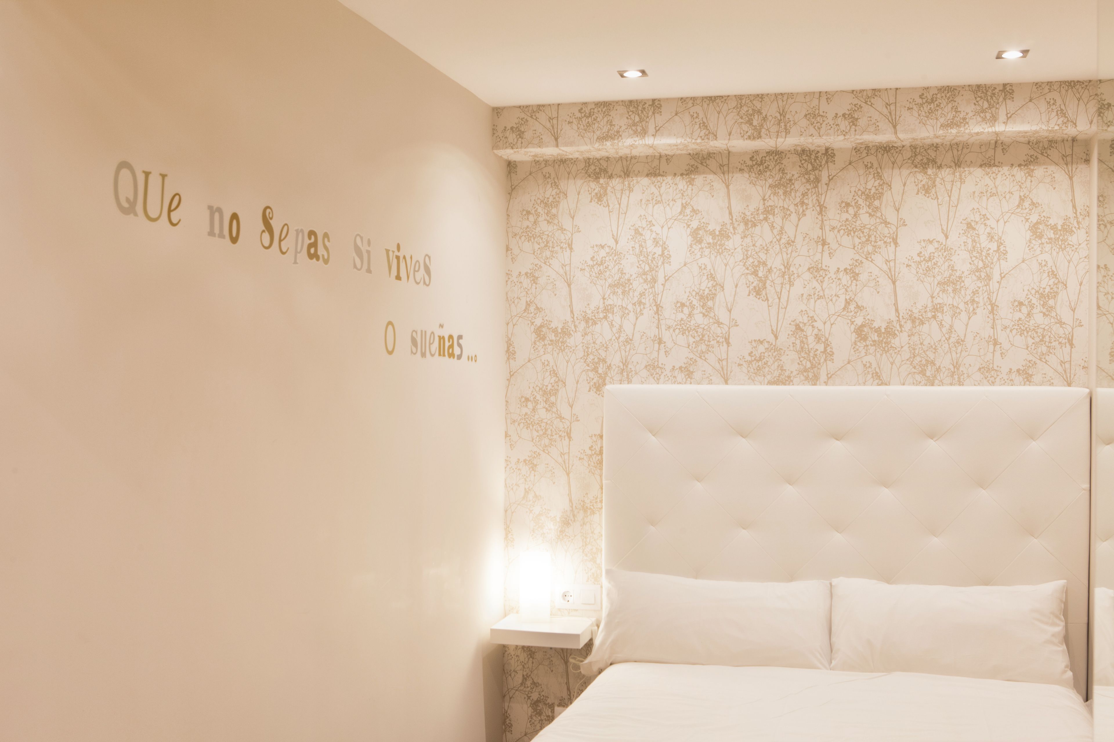 A bedroom with a large bed, a nightstand, and a wall with a floral pattern.