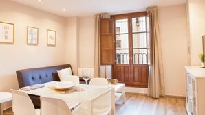Un comedor con una mesa dispuesta para dos personas, un sofá y una ventana con cortinas.