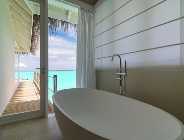 A modern bathroom with a freestanding bathtub, a showerhead, and a view of the ocean through an open door.