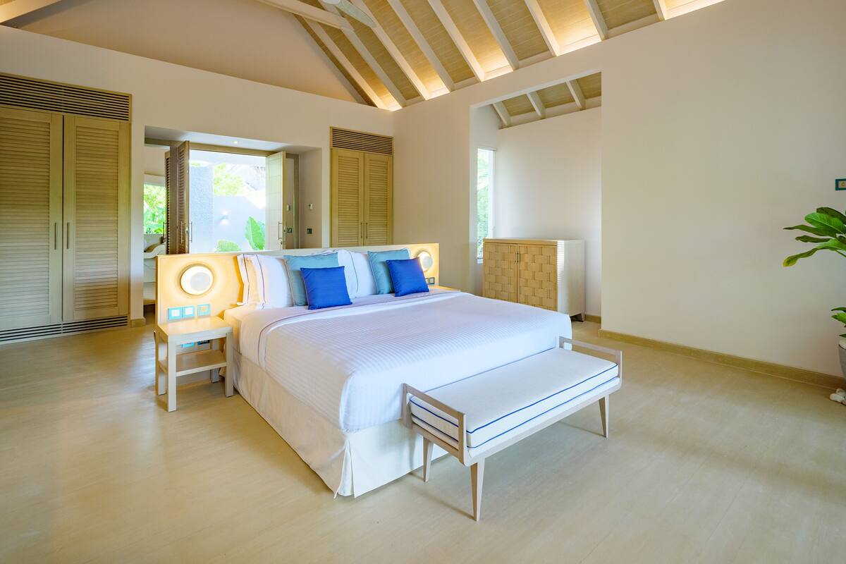 Une chambre à coucher moderne avec un grand lit, une tête de lit en bois et un banc au pied du lit.