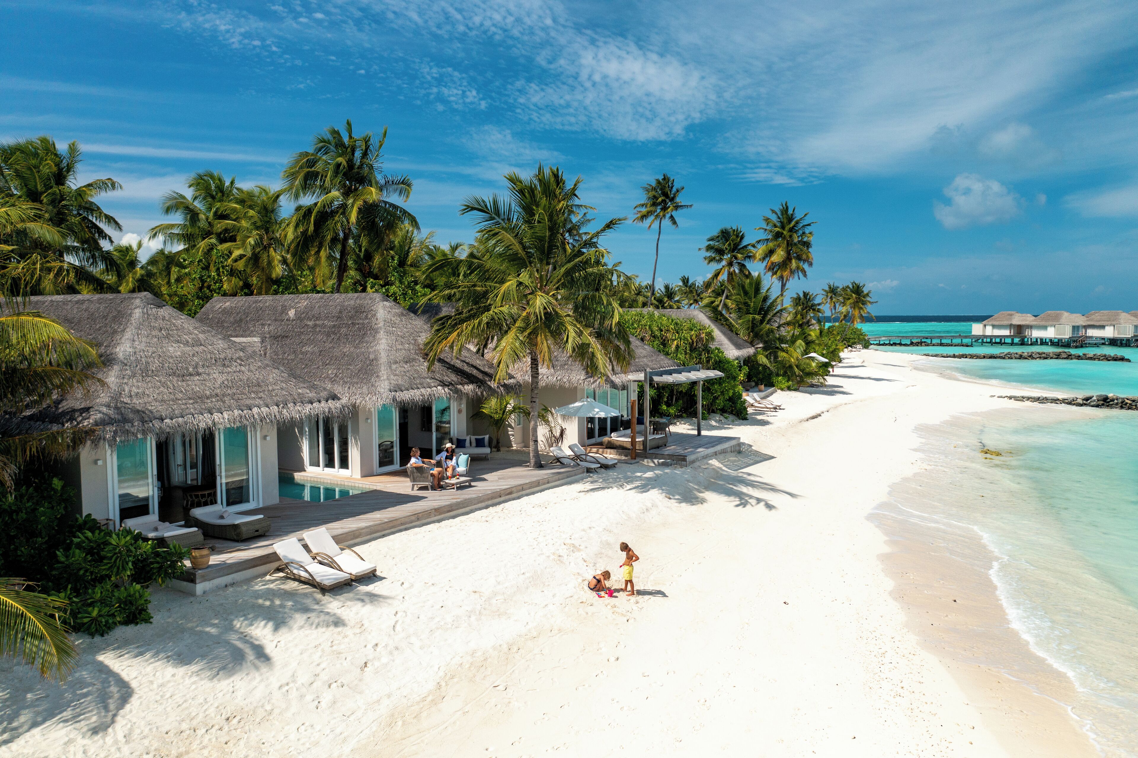 A beach resort with overwater bungalows, a pool area, and a sandy beach.