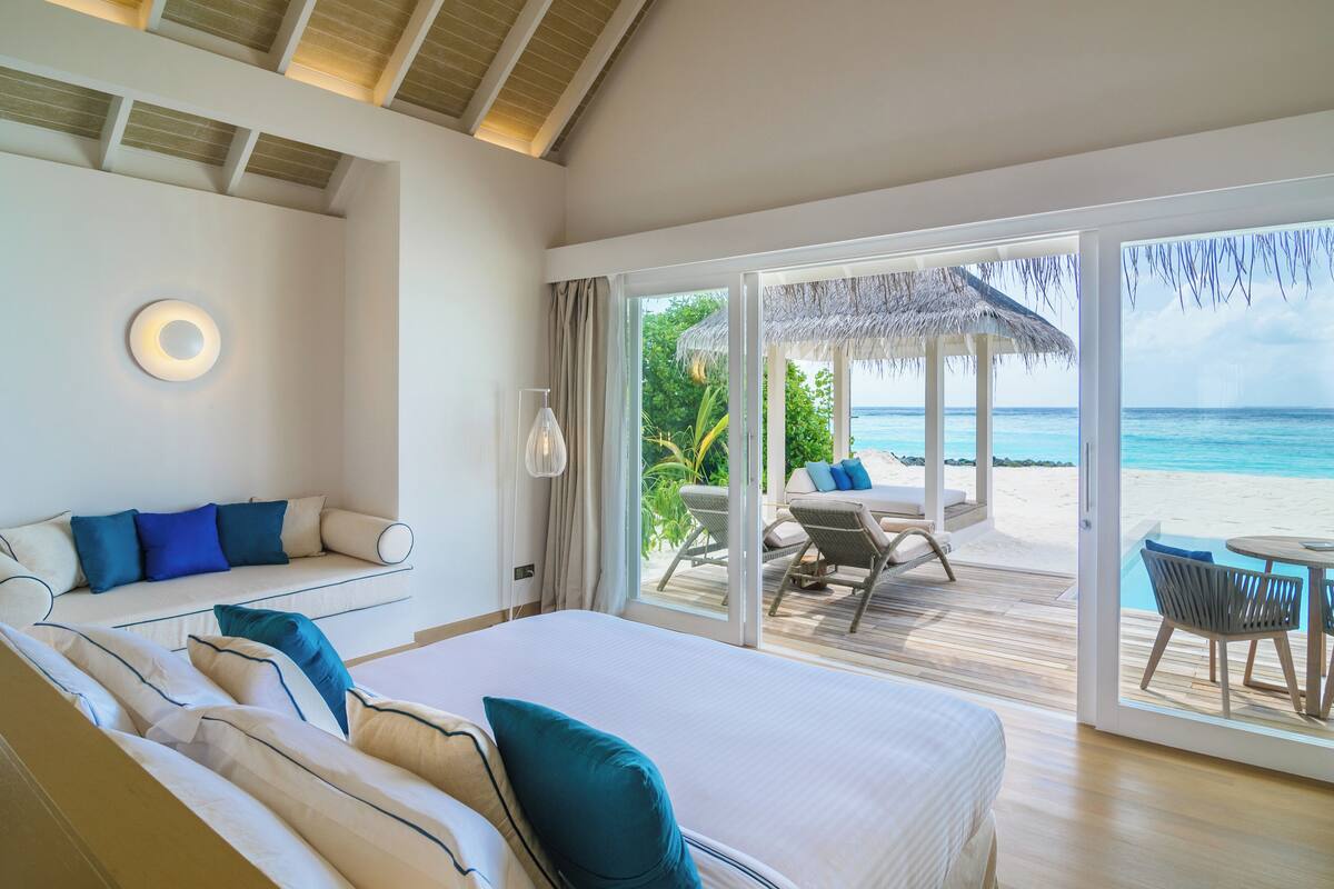 Une chambre dotée d’un grand lit, d’un canapé et offrant une vue sur la plage grâce à une porte-fenêtre coulissante.