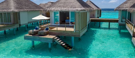 Overwater bungalows with thatched roofs, wooden walkways, and clear turquoise water.