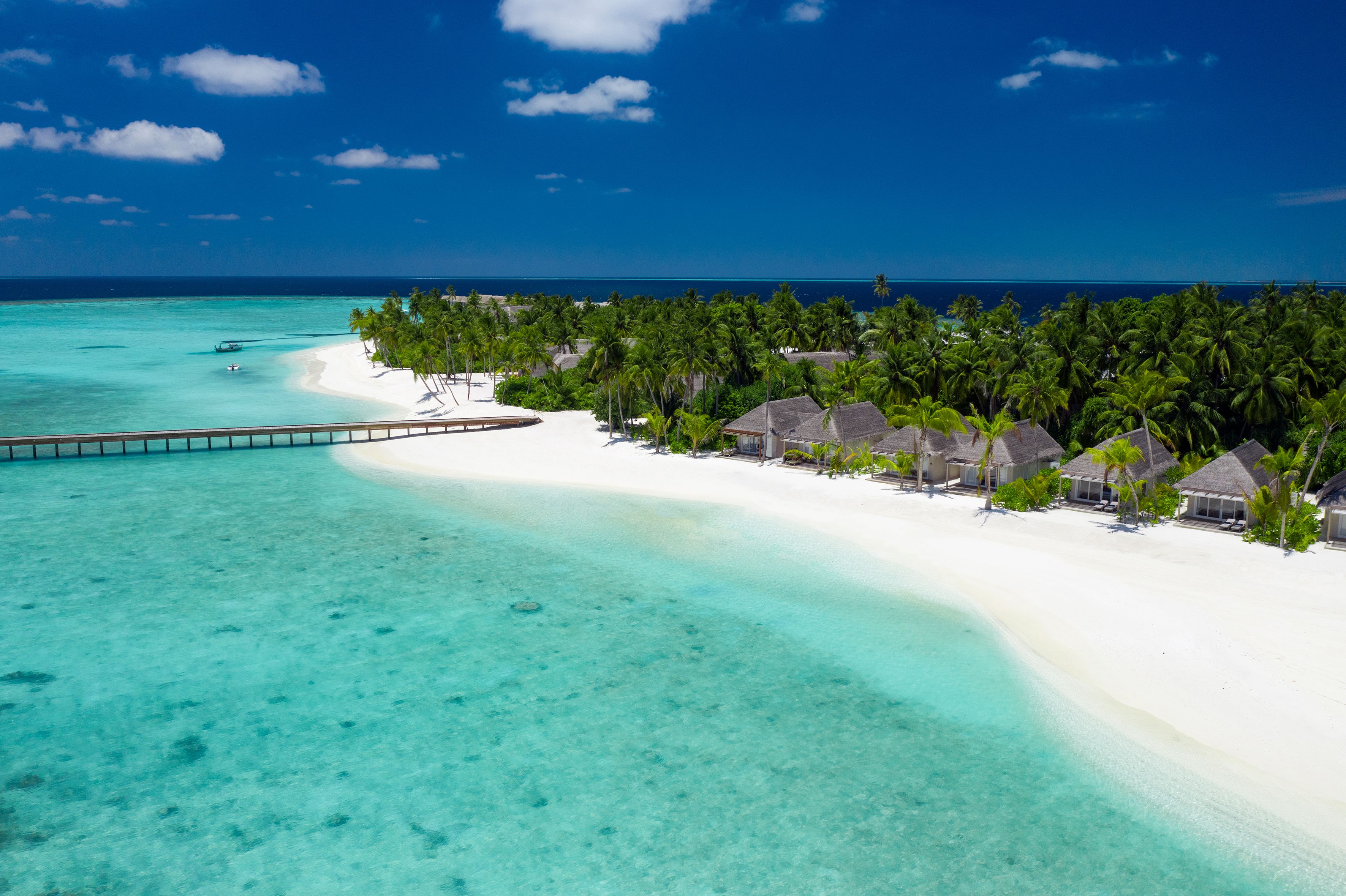Un resort en la playa con bungalows sobre el agua, aguas turquesas cristalinas y una playa de arena blanca.