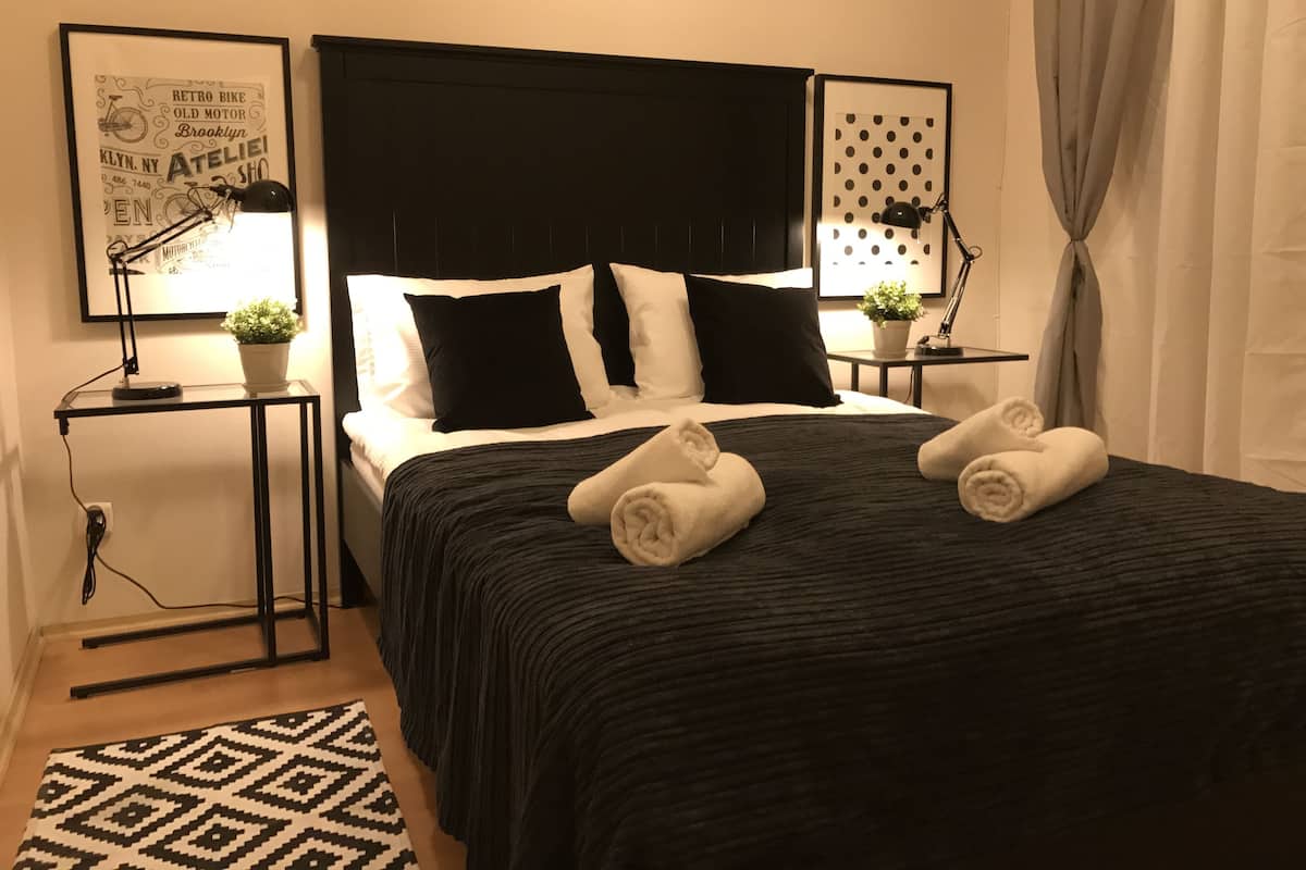 Una cama bien hecha con ropa de cama blanco y negro, dos mesitas de noche con lámparas y una alfombra estampada.