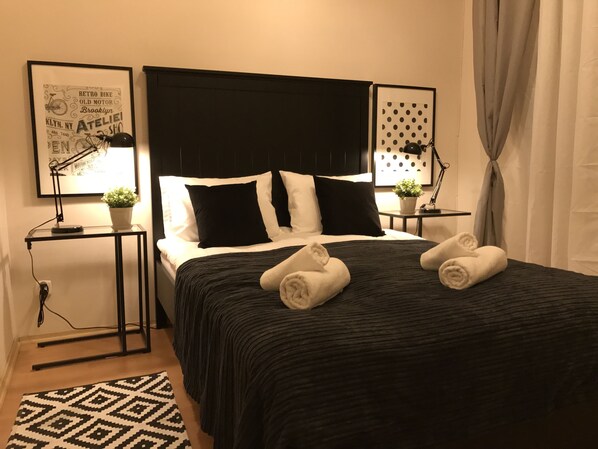 A neatly made bed with black and white bedding, two bedside tables with lamps, and a patterned rug.