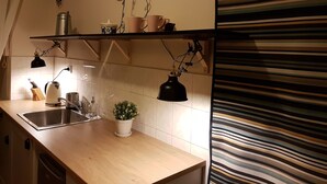 Une cuisine avec un dosseret de carreaux blancs, des plans de travail en bois, un évier, une plante en pot et des luminaires suspendus.