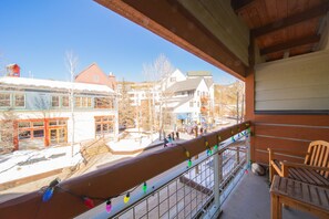 A balcony with a wooden chair, a railing with colorful lights, and a view of buildings and a playground.