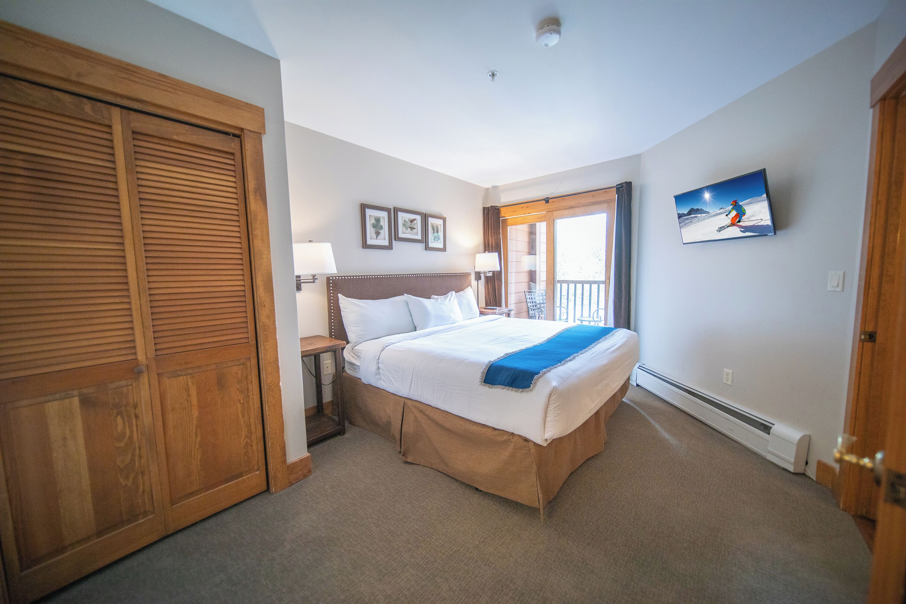 A hotel room with a large bed, wooden wardrobe, and a painting on the wall.