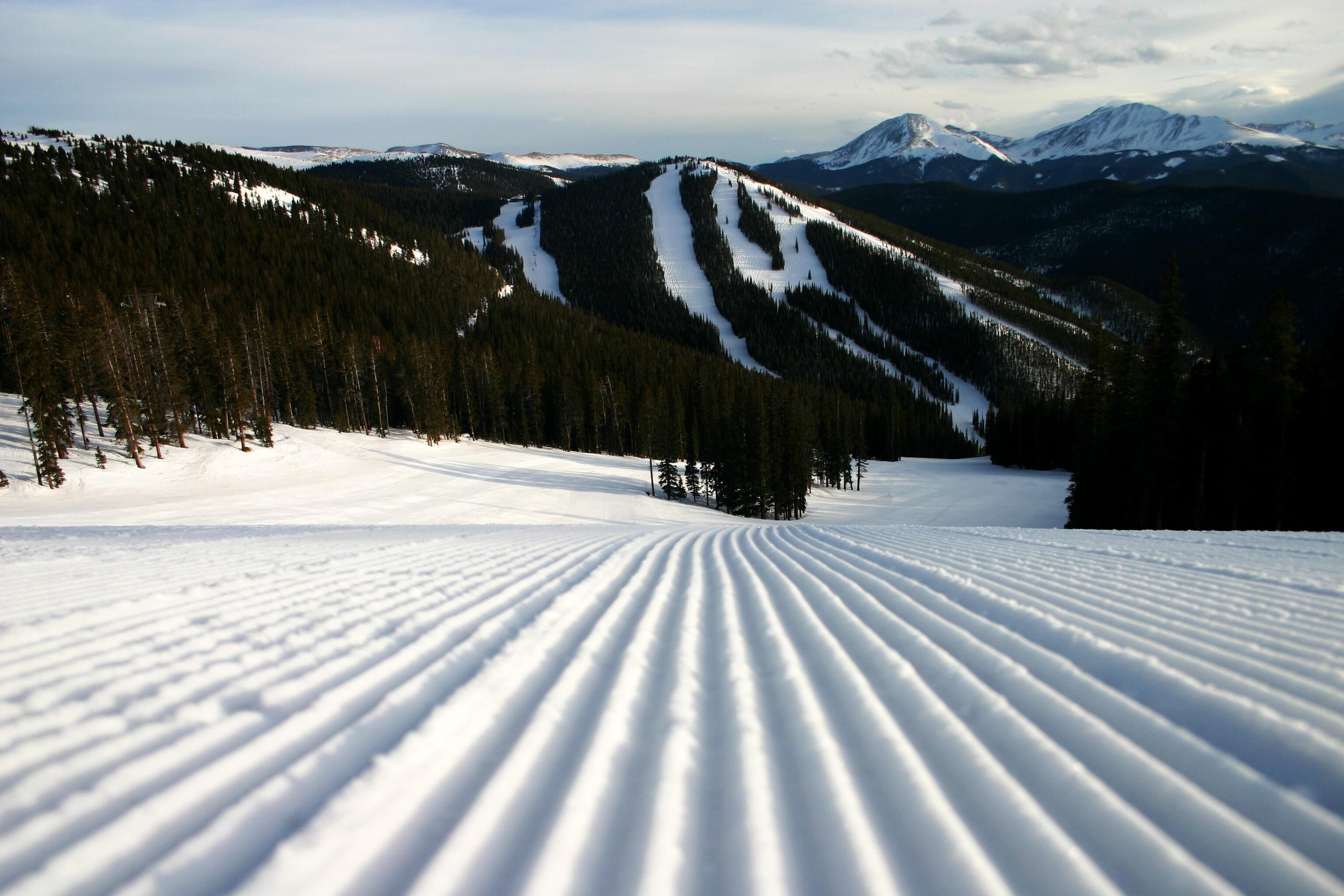 A snow-covered ski slope with a clear path and a mountain range in the background.