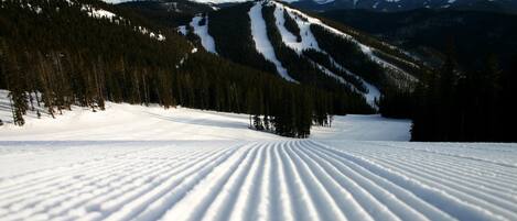 A snow-covered ski slope with a clear path and a mountain range in the background.