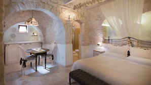 A bedroom with a stone wall, a bed, a bedside table, a chair, and a small table with a lamp. - Romantic Trulli (Alberobello)