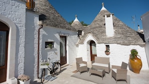 A traditional white building with stone roofs, a bicycle, wicker furniture, and a large vase. - Romantic Trulli (Alberobello)