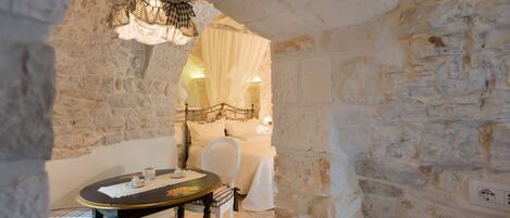 A stone-walled room with a round table, a chair, and a bed with a canopy.
