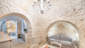A room with stone walls, a chandelier, a bed with a canopy, a sofa, and a dining table with fruit. - Romantic Trulli (Alberobello)
