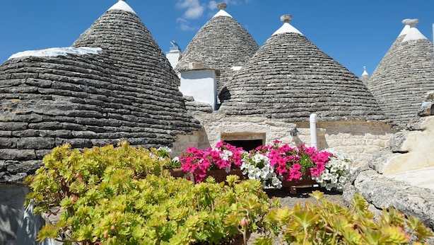 Traditional stone-roofed buildings with a small entrance and colorful flowers in the foreground. - Romantic Trulli (Alberobello)