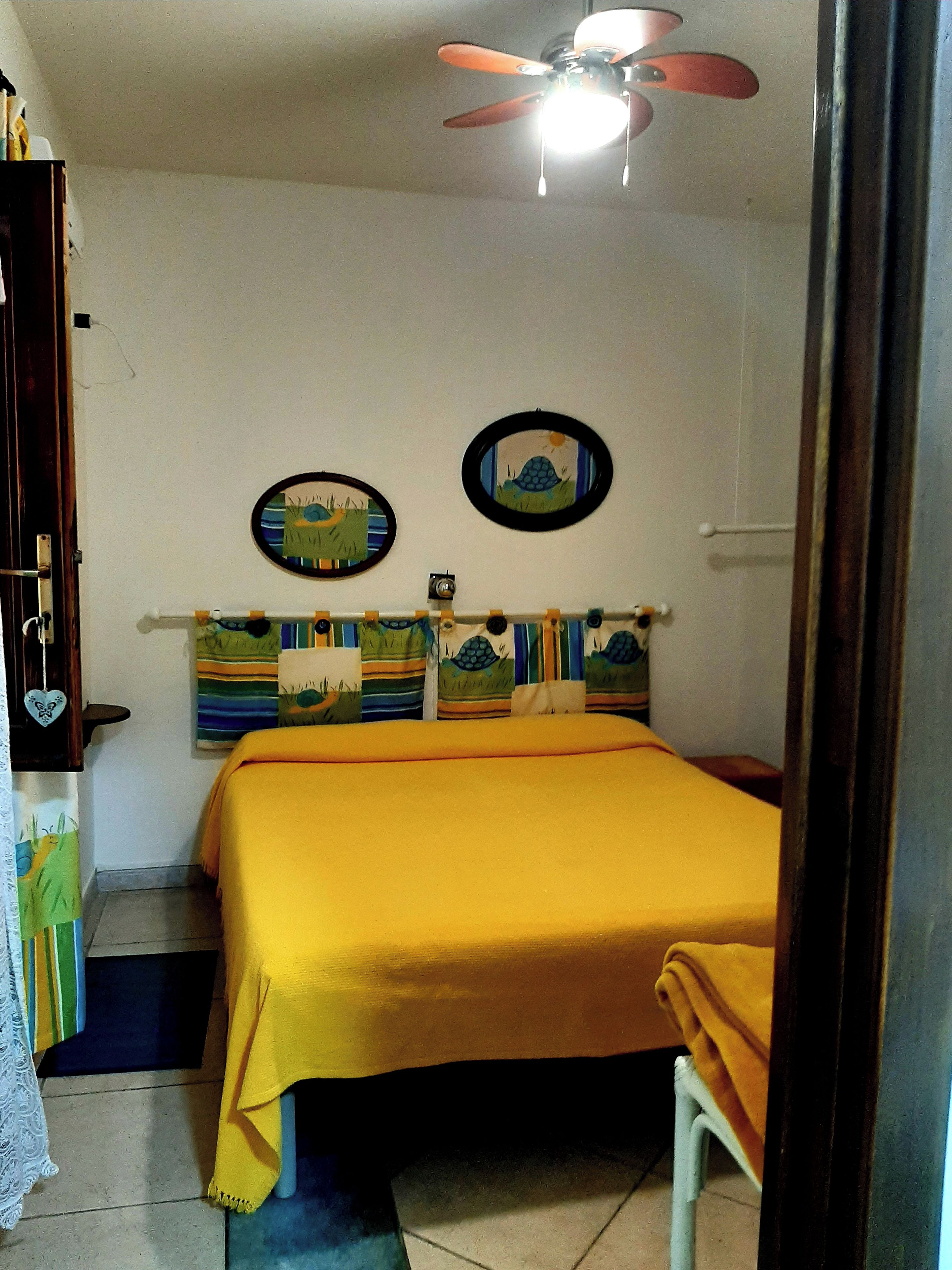 Una habitación con cama, ventilador de techo y dos adornos en la pared.