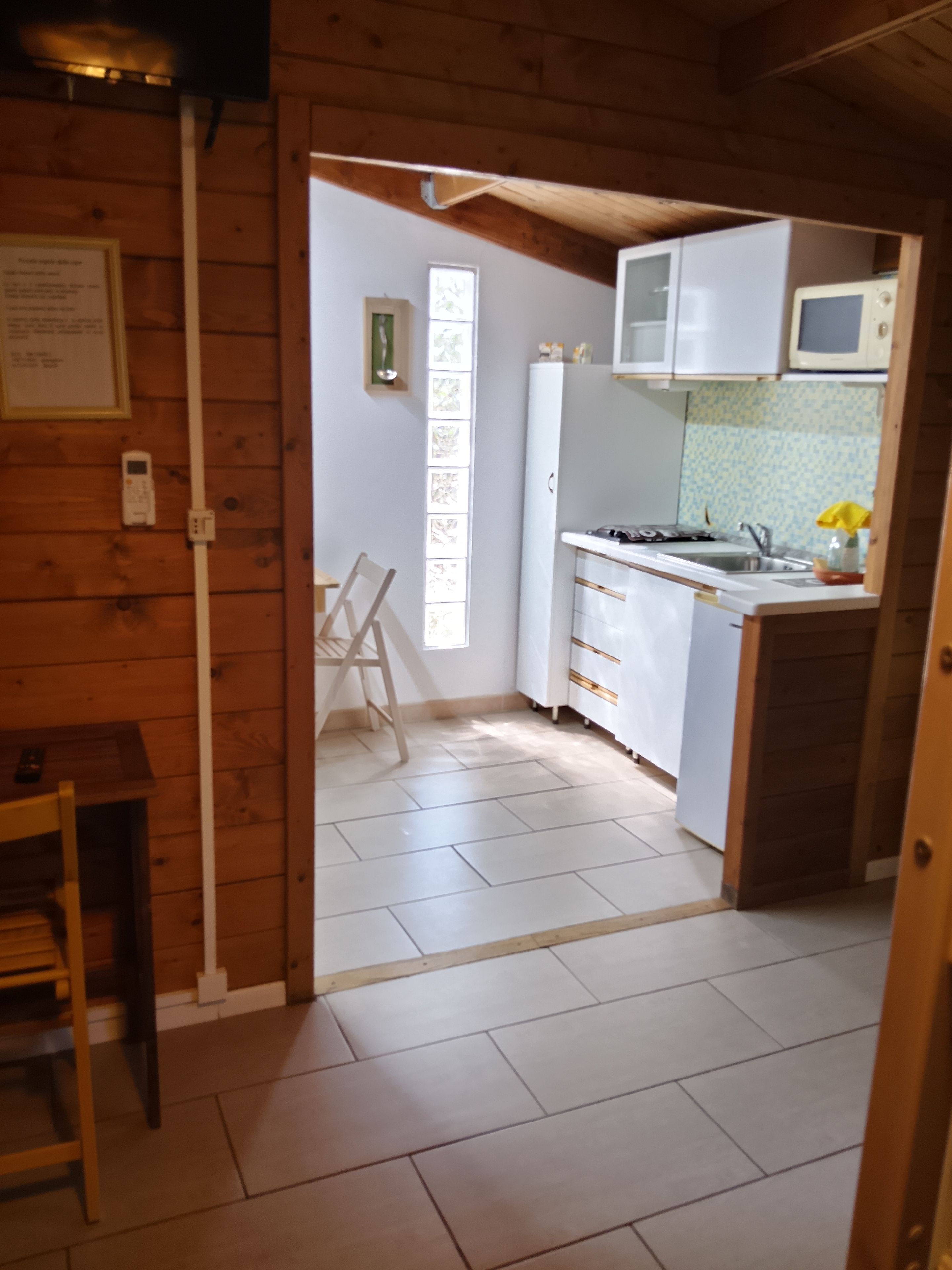 A small kitchen with white cabinets, a microwave, and a sink. There is a window providing natural light and a door leading to another room.