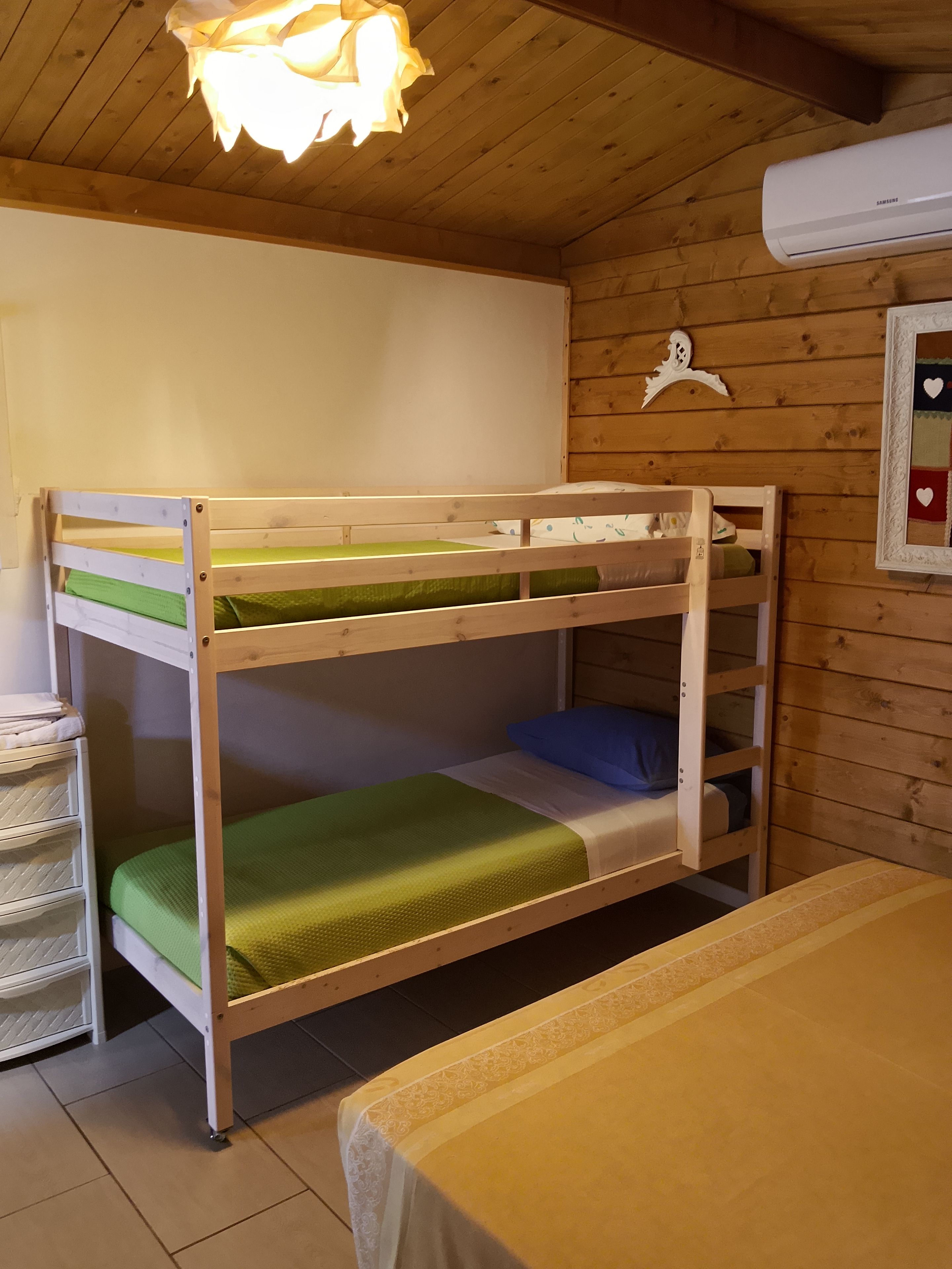Una cama litera con colchón verde, un archivador blanco y un aire acondicionado de pared.