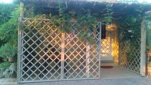A covered outdoor area with a lattice gate, surrounded by greenery and potted plants. - Casa di Campagna Dal Pozzo (Sorso)
