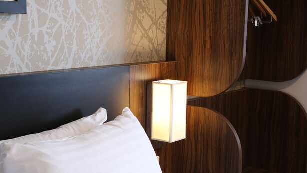 A hotel room with a neatly made bed, a wooden headboard, and a wall-mounted nightstand with a lamp. - Harbour Spring, Peterhead by Marston's Inns (Peterhead)