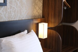 Habitación de hotel con una cama bien hecha, cabecera de madera y mesita de noche con lámpara.