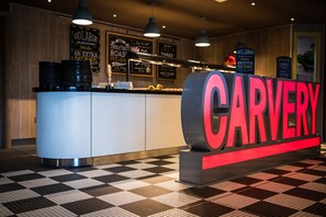 A restaurant counter with a large sign reading "CARVERY" and menu boards advertising dishes like "GOLARGE" and "TRULY ROASTED PIGS".