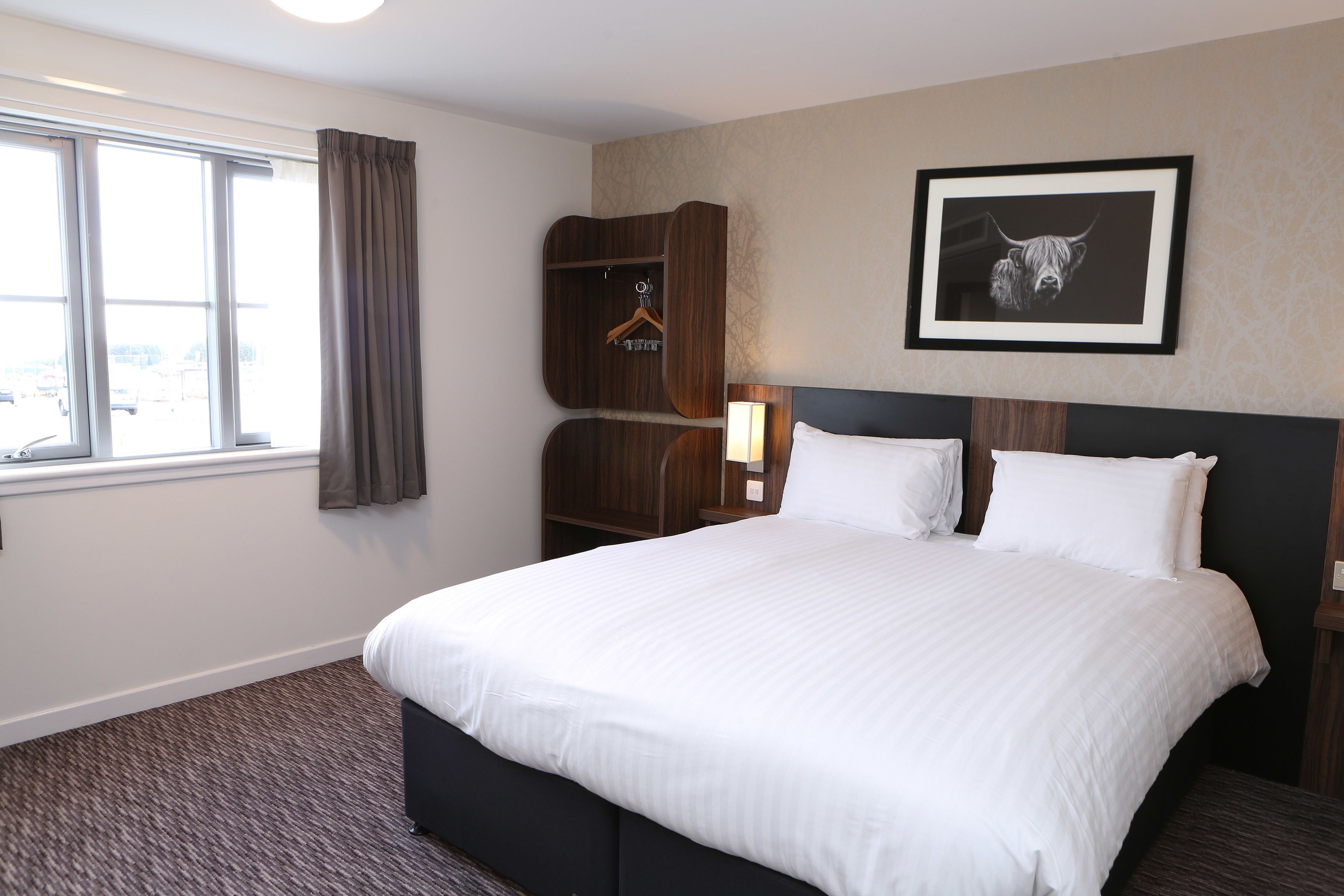 Une chambre d’hôtel avec un grand lit, une armoire, un tableau encadré au mur et une fenêtre avec des rideaux.