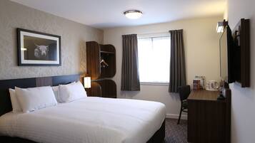 Quarto de hotel com uma cama grande, uma mesa com cadeira, um guarda-roupa, um quadro na parede e uma janela com cortinas.