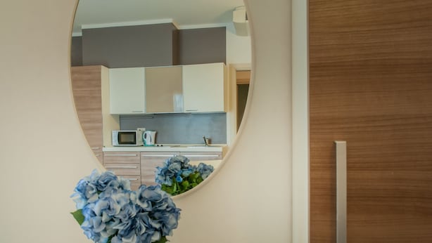 A bathroom with a mirror reflecting a kitchen area, a vase with blue flowers, and a wooden wall. - Residence Art (Rimini)