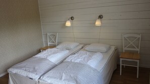 Un lit double avec une couvre-lit à carreaux, deux tables de chevet, deux lampes fixées au mur et une chaise en bois.